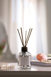 Photo of Reed diffuser and pearl necklace on white table indoors