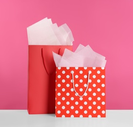 Photo of Gift bags with paper on white table against pink background