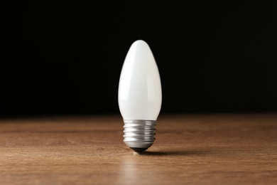 Photo of New modern lamp bulb on wooden table against black background