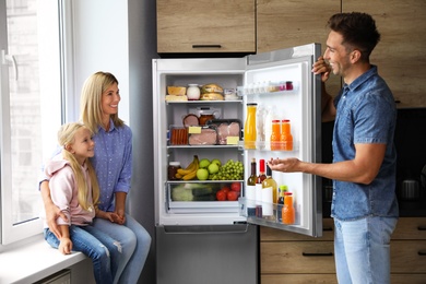 Photo of Happy family near refrigerator full of products in kitchen