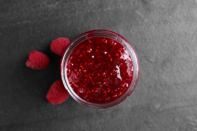 Photo of Delicious jam and fresh raspberries on black slate table, top view