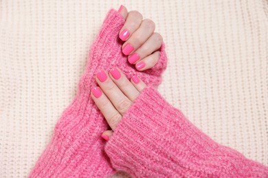 Photo of Woman showing her manicured hands with pink nail polish on knitted blanket, top view