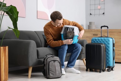 Photo of Travel with pet. Man holding carrier with cute cat on sofa at home