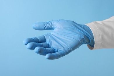 Photo of Doctor wearing medical glove holding something on light blue background, closeup