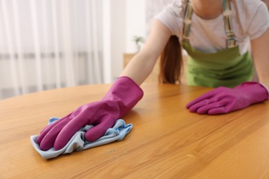 Photo of Woman with microfiber cloth cleaning wooden table in room, closeup