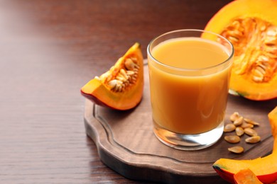 Photo of Tasty pumpkin juice in glass and cut pumpkin on wooden table. Space for text
