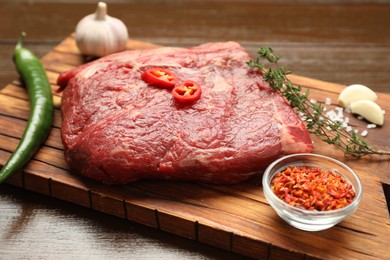 Fresh raw beef cut with spices on wooden table, closeup