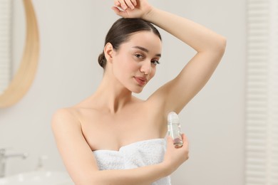 Photo of Beautiful young woman applying deodorant in bathroom