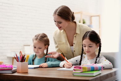 Mother helping her daughters with homework at table indoors