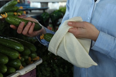 Photo of Woman putting cucumber into cotton eco bag at wholesale market, closeup. Life without plastic