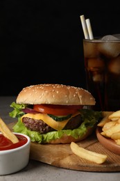 Photo of Delicious burger, soda drink and french fries served on grey table, closeup