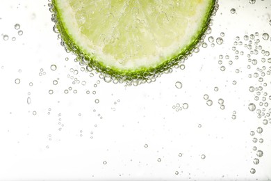 Photo of Juicy lime slice in soda water against white background, closeup. Space for text