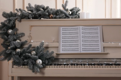 White piano with festive decor and note sheets indoors. Christmas music