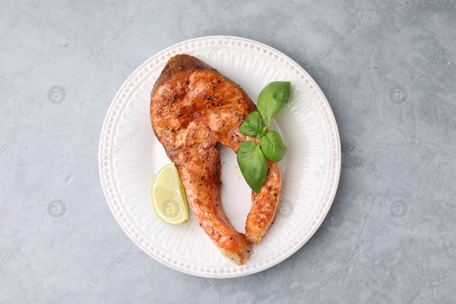 Photo of Freshly cooked fish, lime and basil on grey table, top view