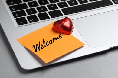 Image of Sticky note with word Welcome and candy on laptop, closeup