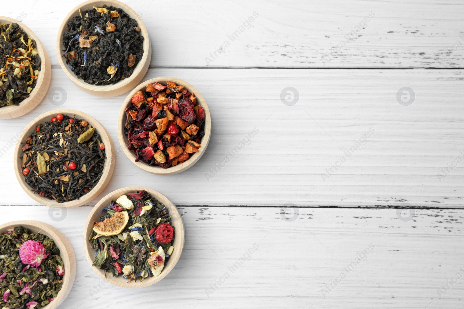 Photo of Different kinds of dry herbal tea in bowls on white wooden table, flat lay