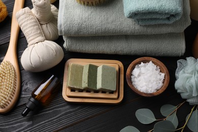 Composition with different spa products and eucalyptus branches on black wooden table, above view