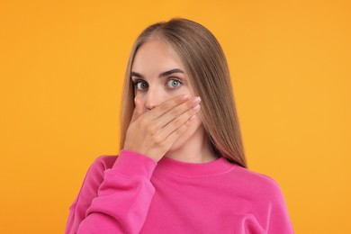 Photo of Embarrassed woman covering mouth with hand on orange background