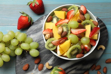 Photo of Tasty fruit salad in bowl and ingredients on light blue wooden table, flat lay