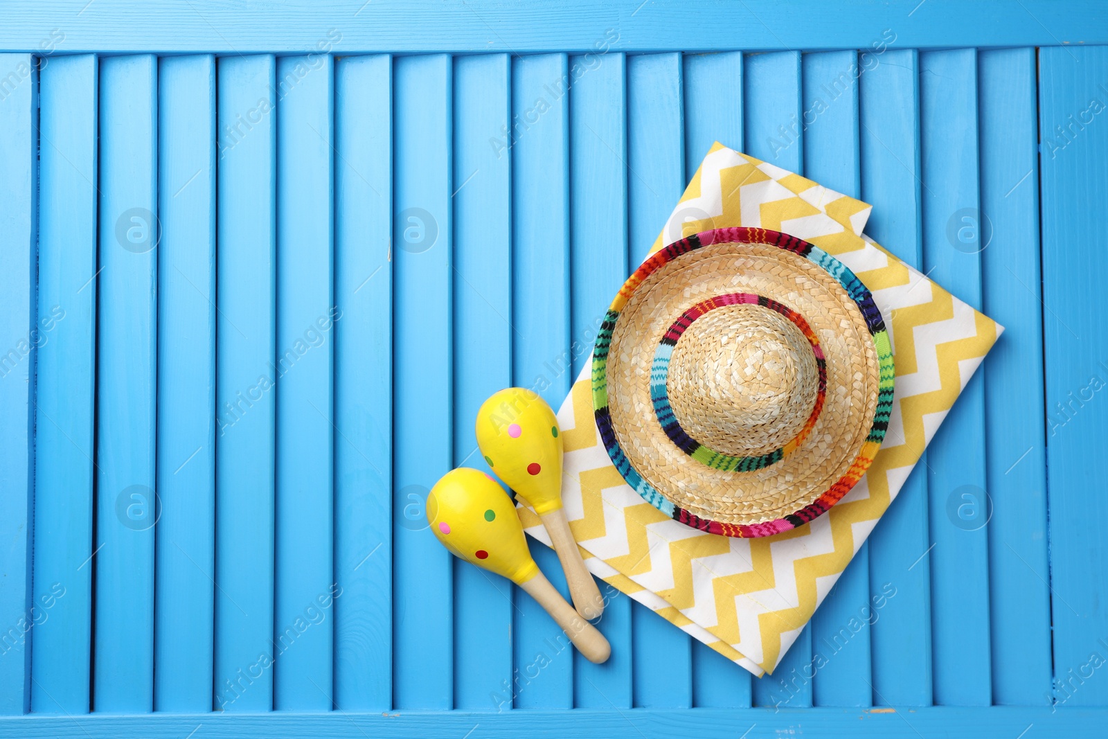 Photo of Mexican sombrero hat, towel and maracas on blue wooden surface, top view. Space for text