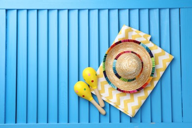 Mexican sombrero hat, towel and maracas on blue wooden surface, top view. Space for text