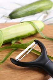 Photo of Fresh cucumbers, peels and peeler on wooden board, closeup