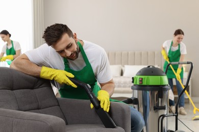 Photo of Professional janitor in uniform vacuuming armchair indoors