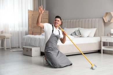Photo of Man with mop singing while cleaning in bedroom
