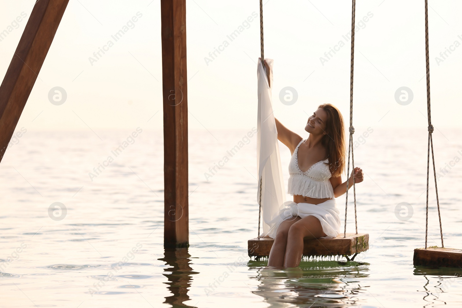 Photo of Young woman enjoying sunrise on swing over water