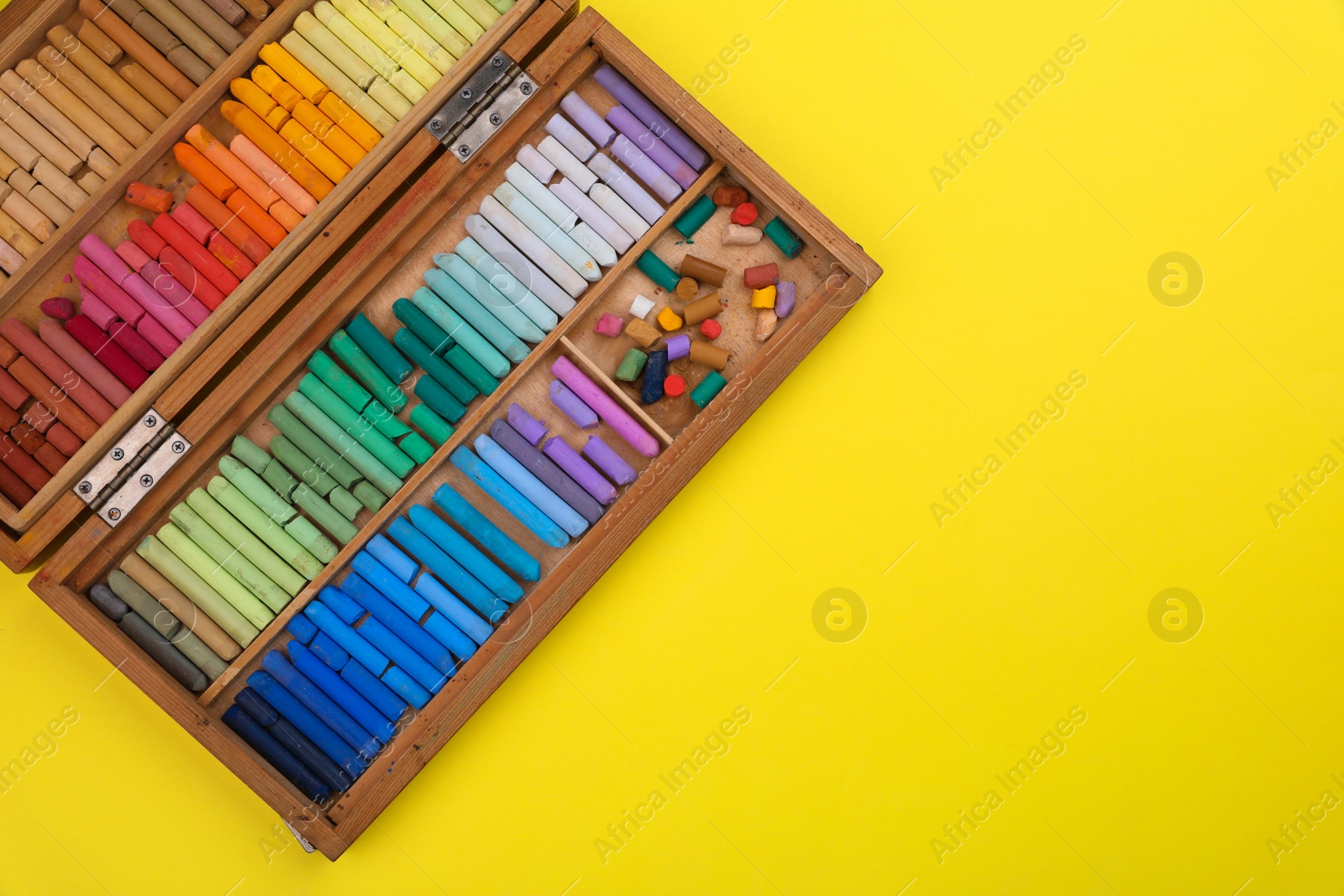 Photo of Set of soft pastels in wooden box on yellow background, top view with space for text. Drawing material