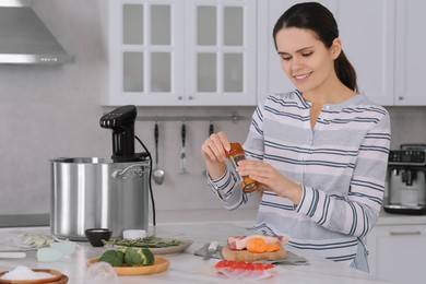 Photo of Woman grinding pepper onto meat near pot with sous vide cooker in kitchen. Thermal immersion circulator