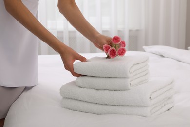 Photo of Chambermaid putting flowers with fresh towels in hotel room, closeup