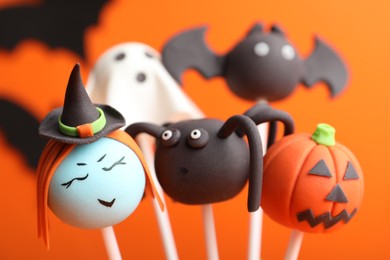 Photo of Delicious Halloween themed cake pops on orange background, closeup