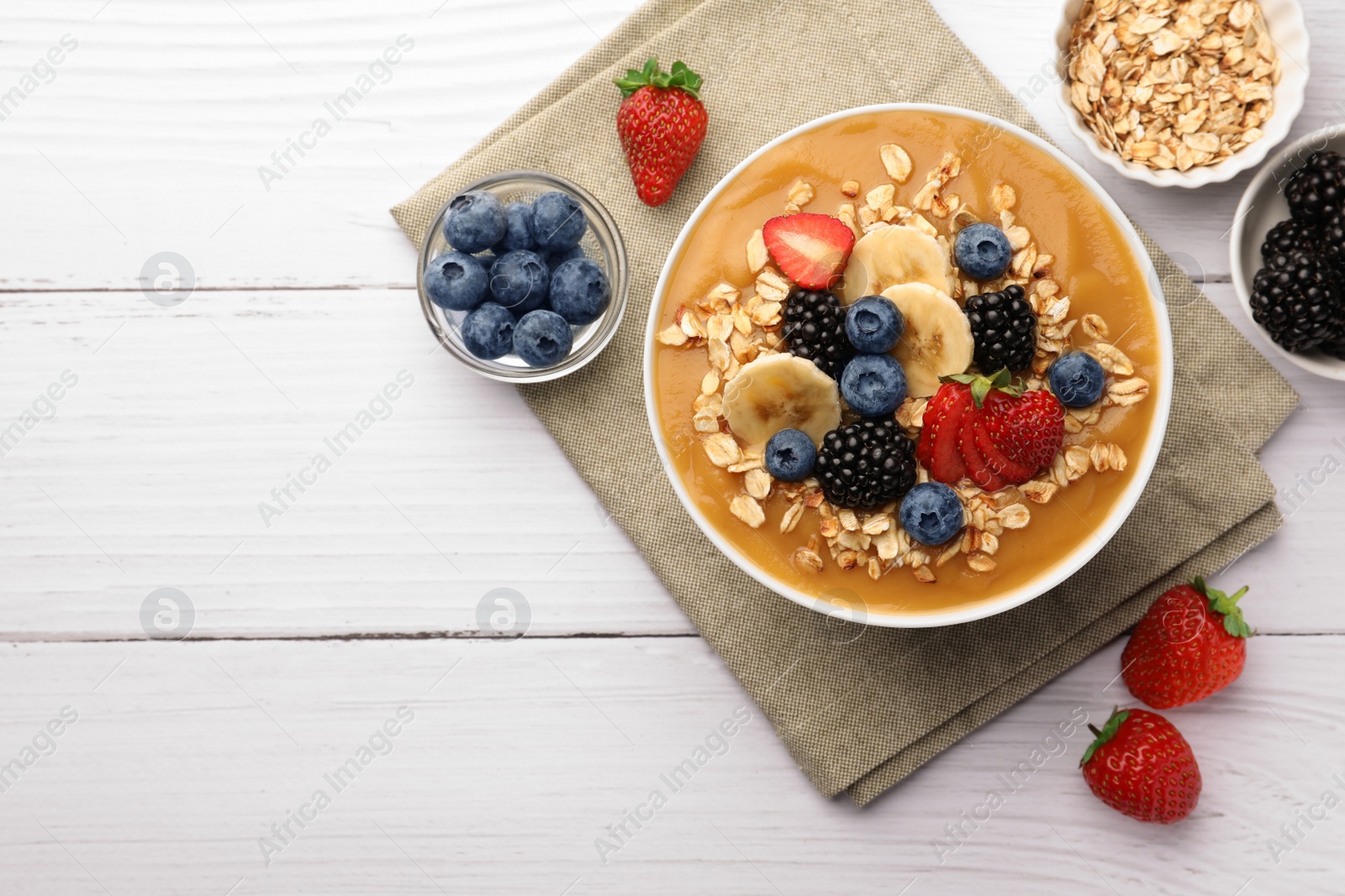 Photo of Delicious smoothie bowl with fresh berries, banana and oatmeal on white wooden table, flat lay. Space for text
