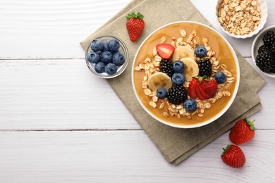 Delicious smoothie bowl with fresh berries, banana and oatmeal on white wooden table, flat lay. Space for text