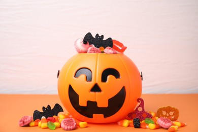 Photo of Halloween trick or treat bucket with different sweets on orange table