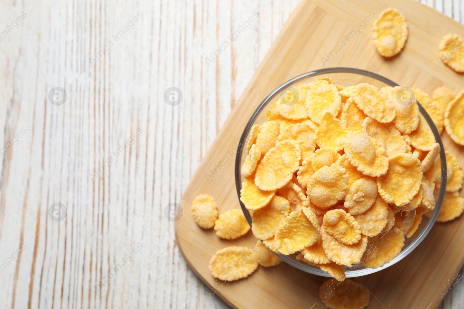 Photo of Glass bowl of tasty crispy corn flakes on white wooden table, top view. Space for text