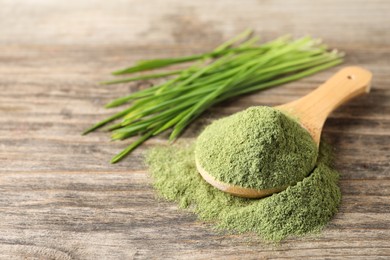 Photo of Wheat grass powder in spoon on wooden table, closeup. Space for text