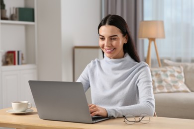 Happy woman working with laptop at wooden desk in room