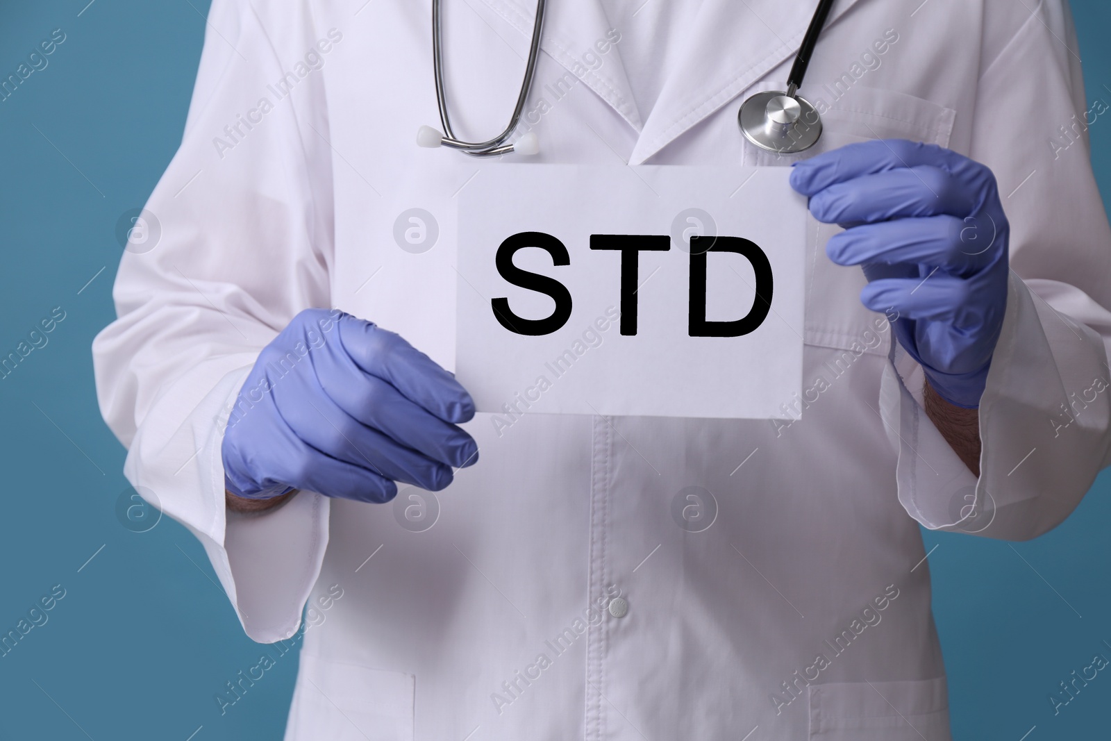 Photo of Doctor holding sheet of paper with abbreviation STD on light blue background, closeup