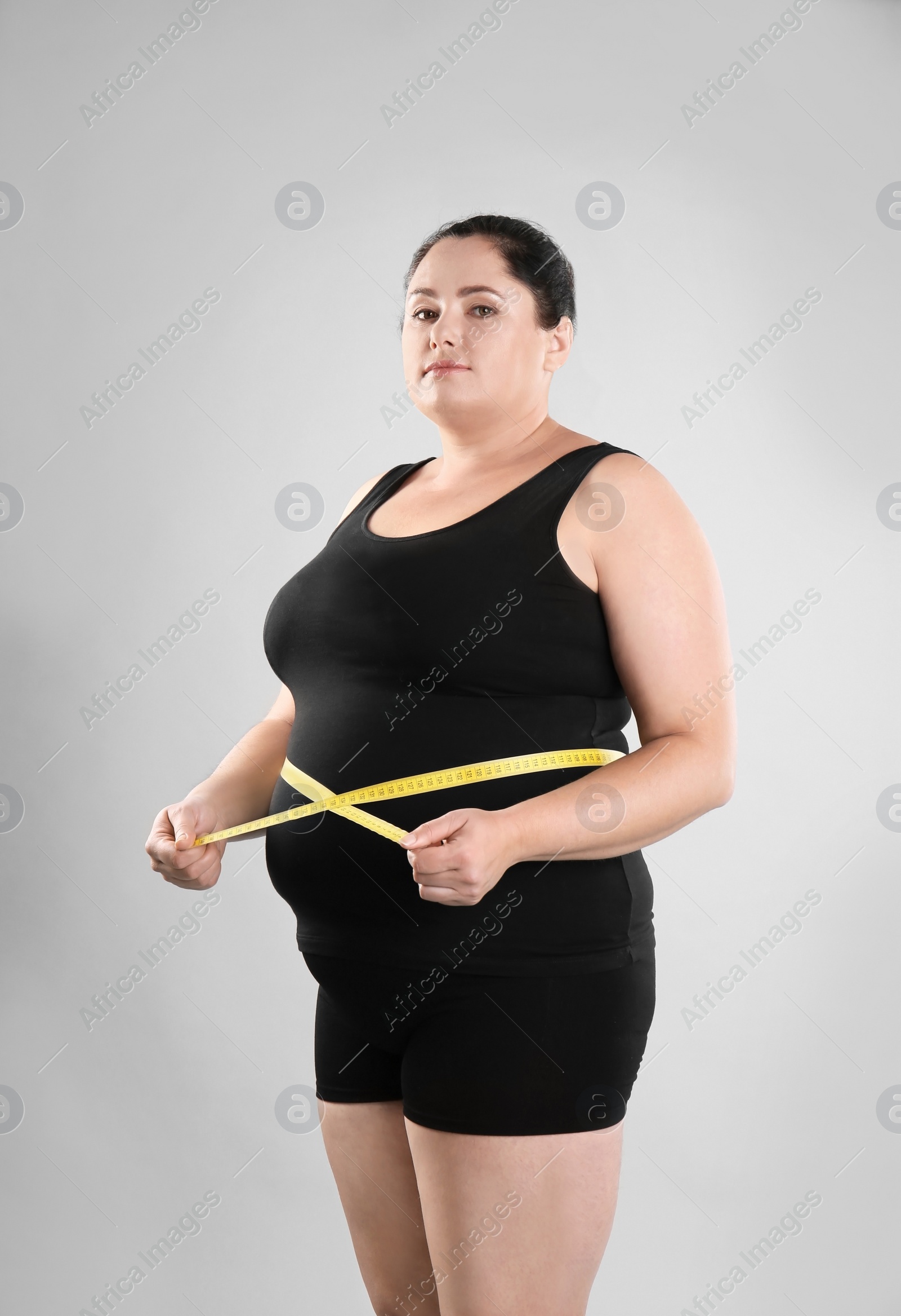 Photo of Fat woman with measuring tape on grey background. Weight loss