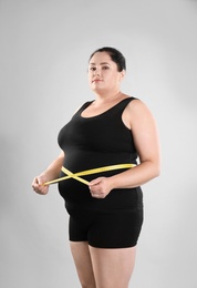 Fat woman with measuring tape on grey background. Weight loss