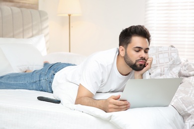 Photo of Lazy young man with laptop on bed at home