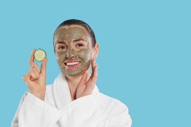 Beautiful woman with clay mask holding piece of cucumber on light blue background, space for text