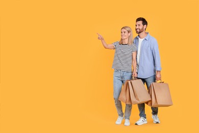 Photo of Family shopping. Happy couple with paper bags on orange background. Space for text