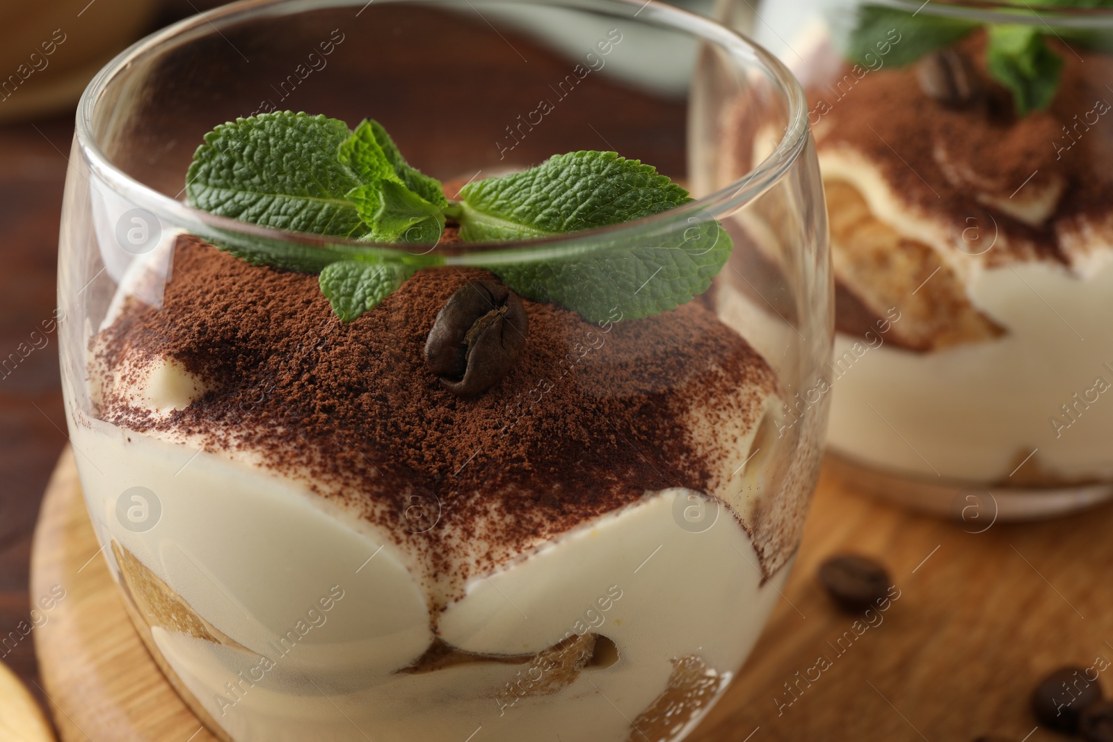 Photo of Delicious tiramisu in glasses, mint leaves and coffee beans on table, closeup