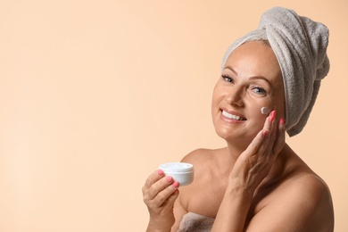 Photo of Portrait of beautiful mature woman with perfect skin holding jar of cream on beige background. Space for text