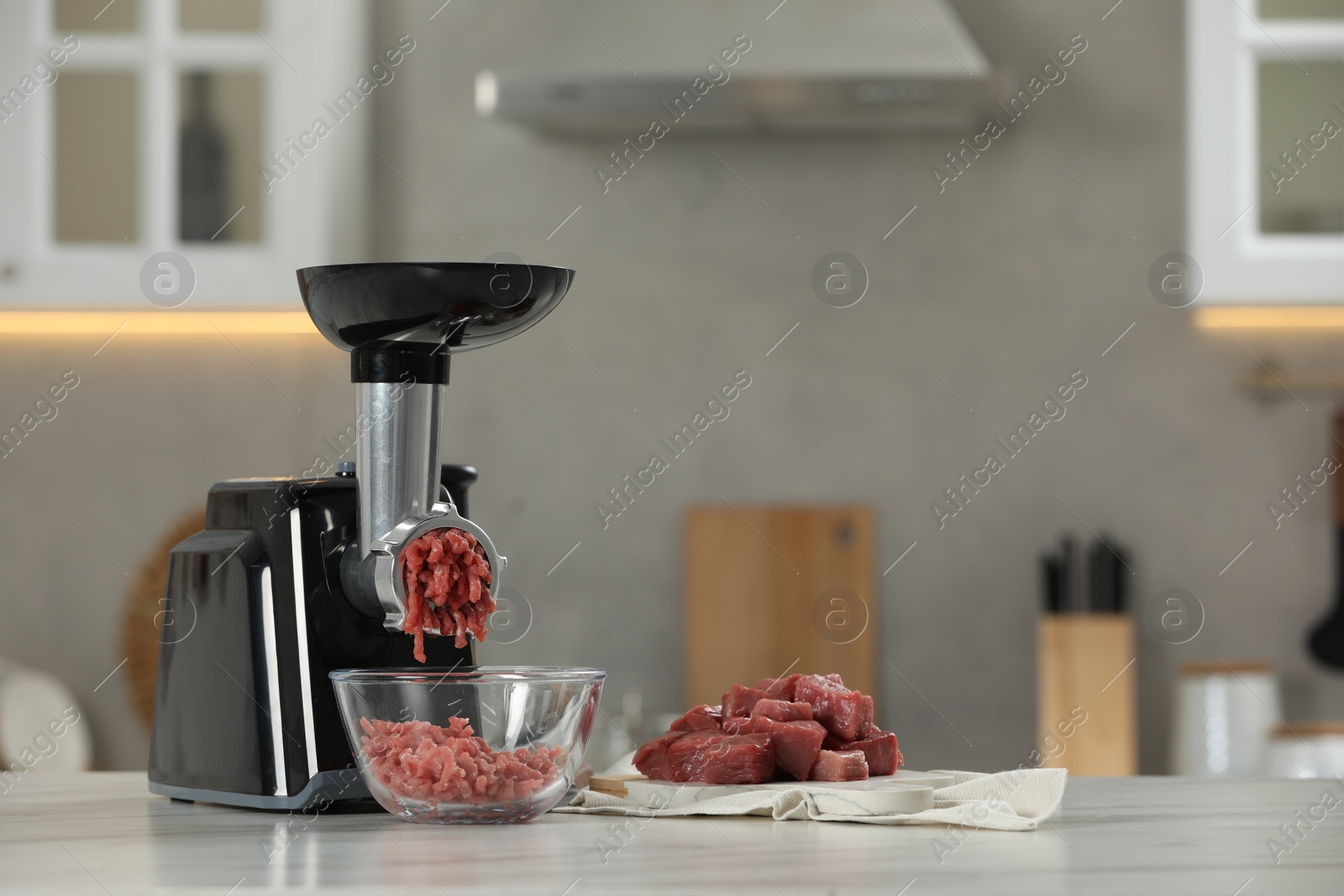 Photo of Electric meat grinder with beef mince on white table in kitchen, space for text