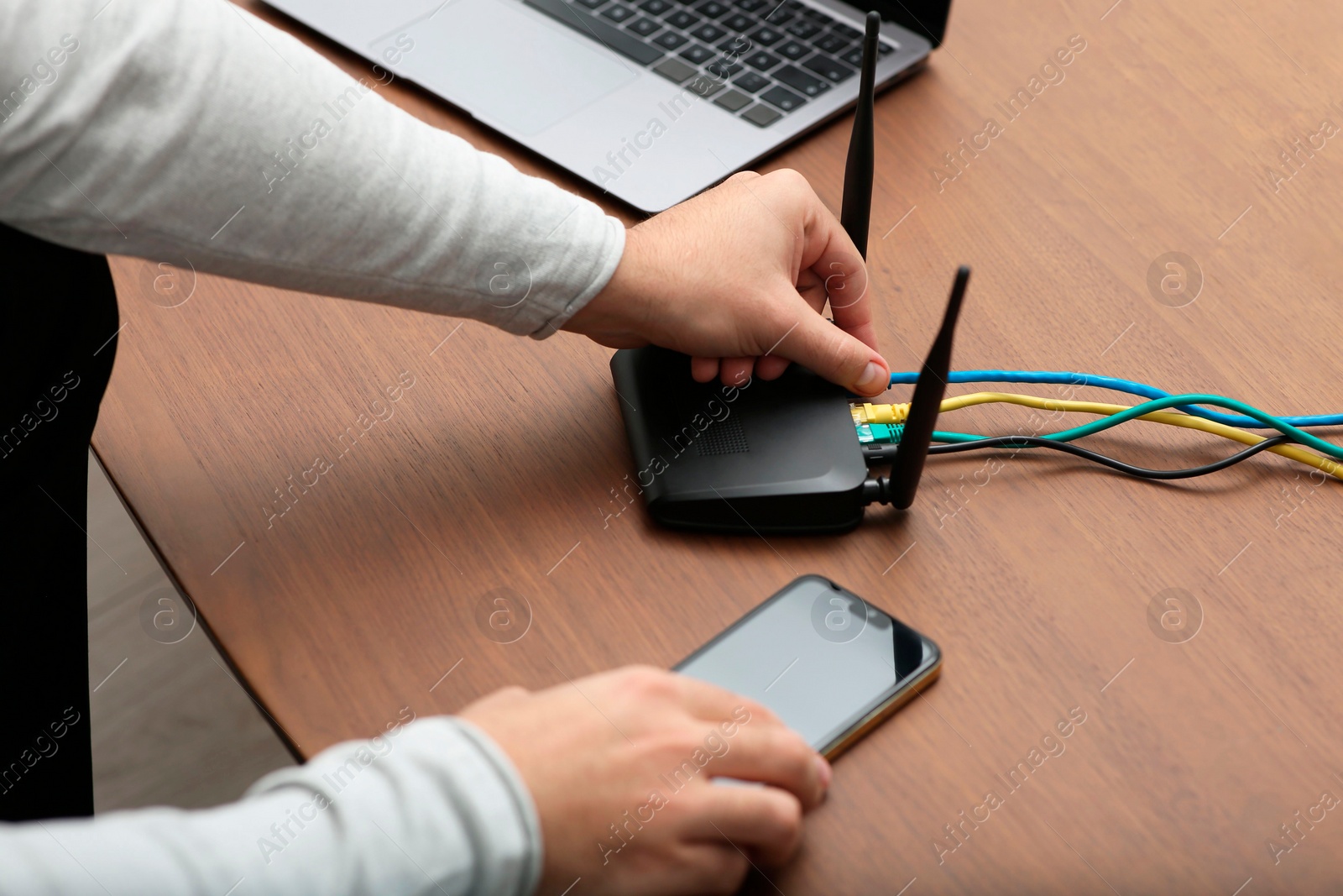 Photo of Man with smartphone connecting to internet via Wi-Fi router at wooden table, closeup