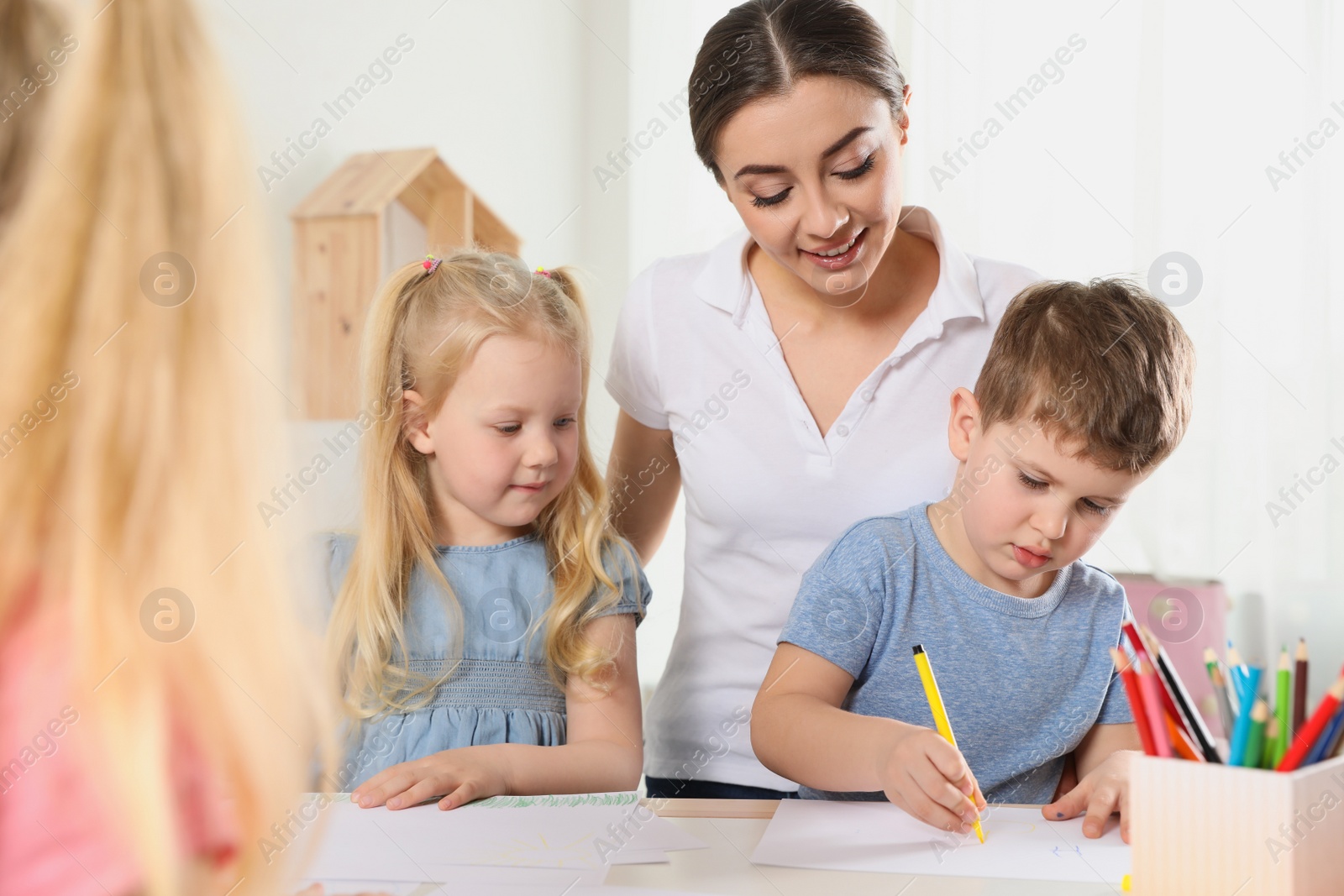 Photo of Little children with kindergarten teacher drawing at table indoors. Learning and playing